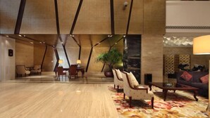 A spacious lobby with a high ceiling, a seating area with chairs and a table, and a large plant. - Zhongshan Yihe Junli Hotel (Holiday Plaza Branch) (Zhongshan)