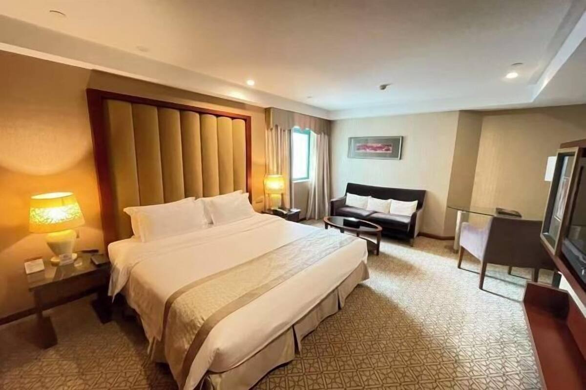 A hotel room with a large bed, a sofa, a TV, and a lamp.