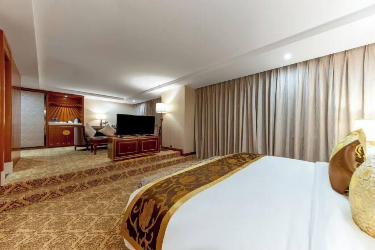 A hotel room with a large bed, a television, a desk with a chair, and a carpeted floor.