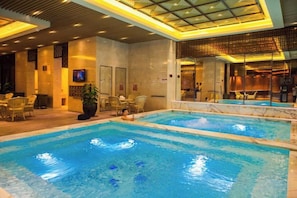 A hotel swimming pool area with multiple pools, lounge chairs, and a television screen. - Zhongshan Yihe Junli Hotel (Holiday Plaza Branch) (Zhongshan)
