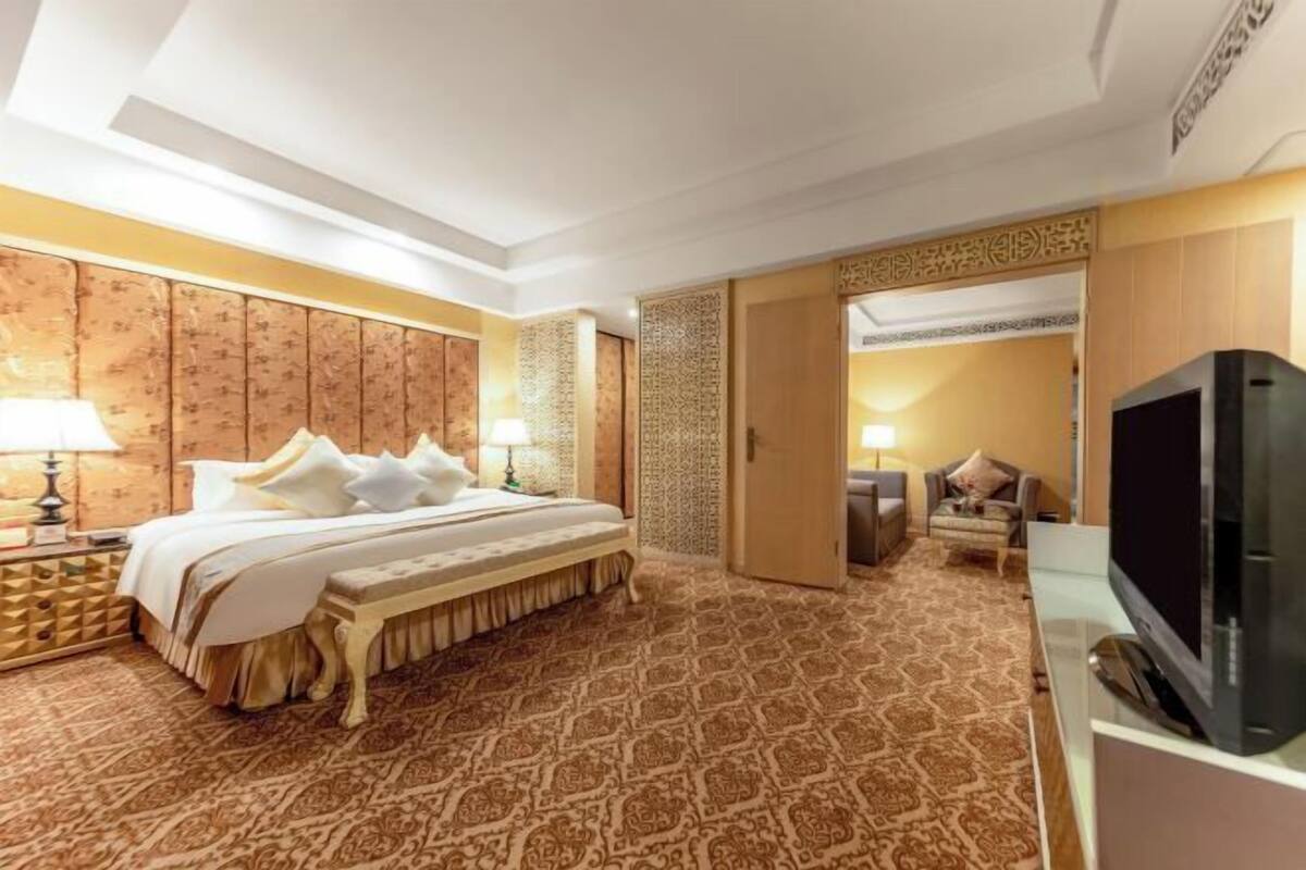 A hotel room with a large bed, a television, and a patterned carpet.