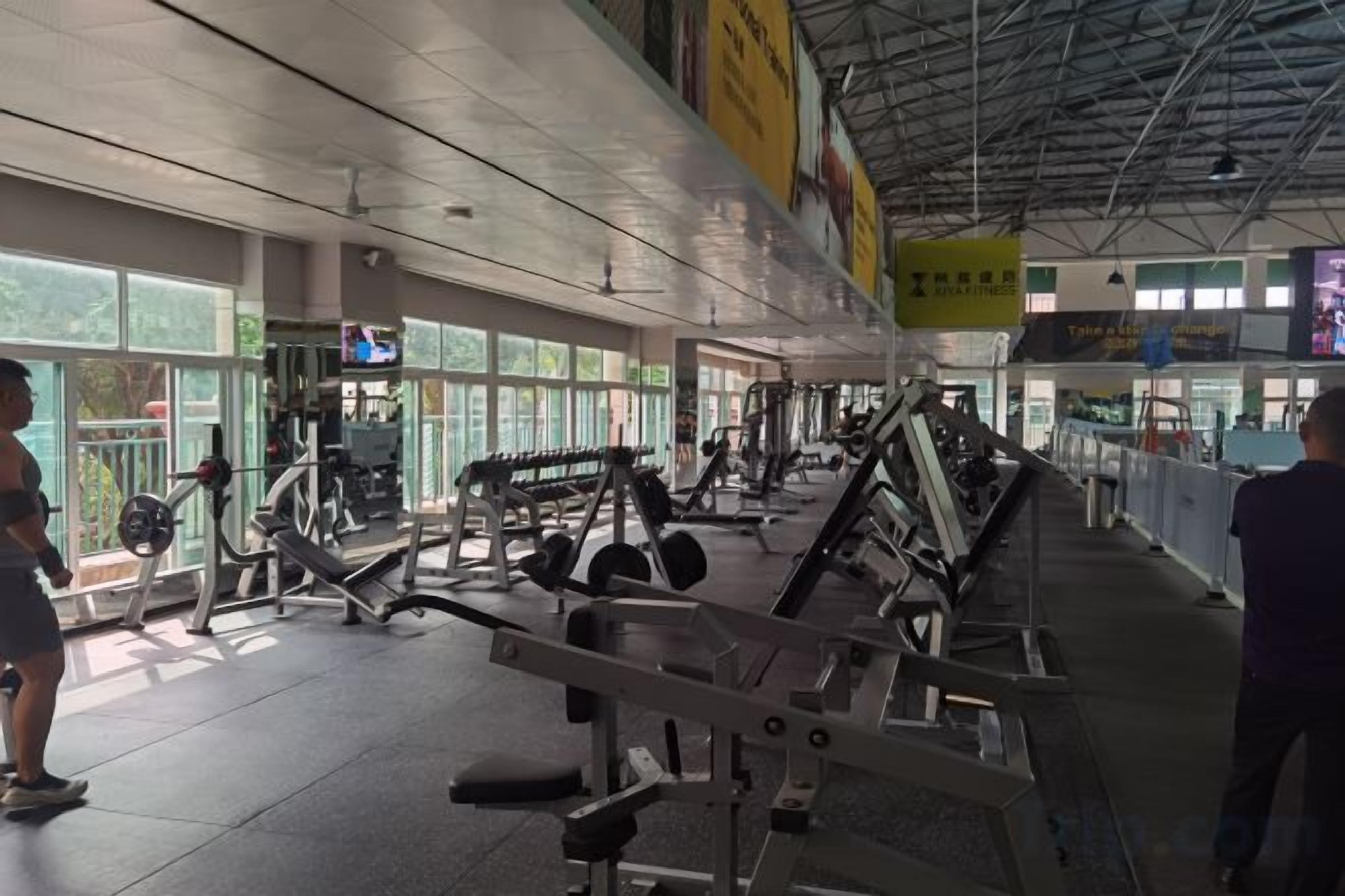 Ein Fitnessstudio mit unterschiedlichen Trainingsgeräten, großen Fenstern und einer hohen Decke.