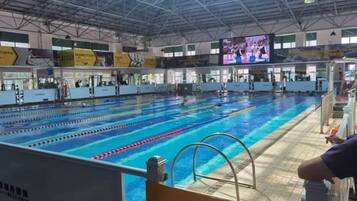 An indoor swimming pool with multiple lanes, a diving platform, and a large screen displaying an event.