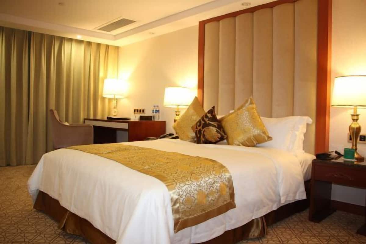 A hotel room with a large bed, two bedside tables, a desk, a chair, and a curtain.