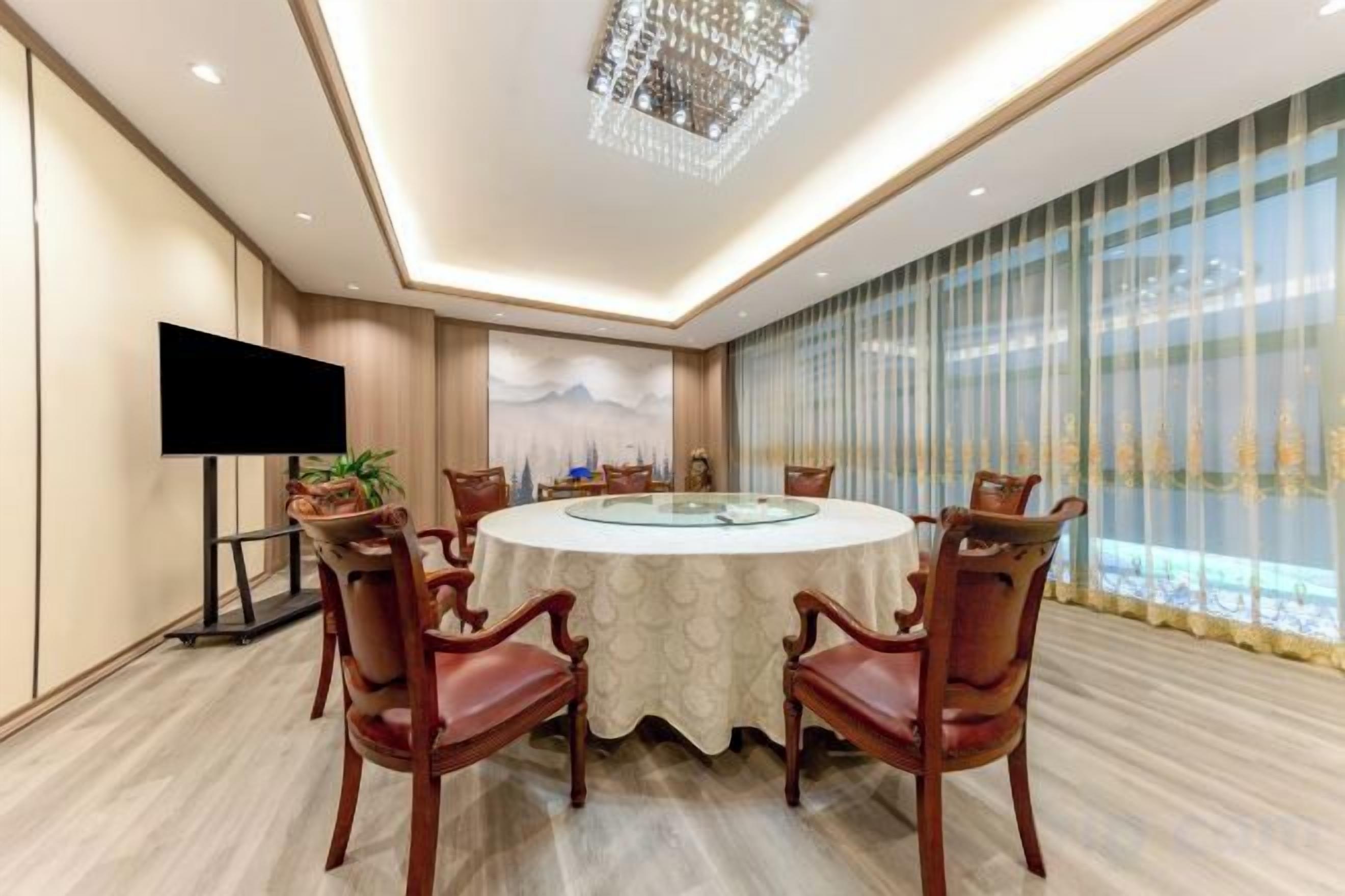 A conference room with a round table, chairs, a flat-screen TV, and a large window with curtains.