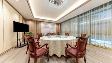 A conference room with a round table, chairs, a flat-screen TV, and a large window with curtains.