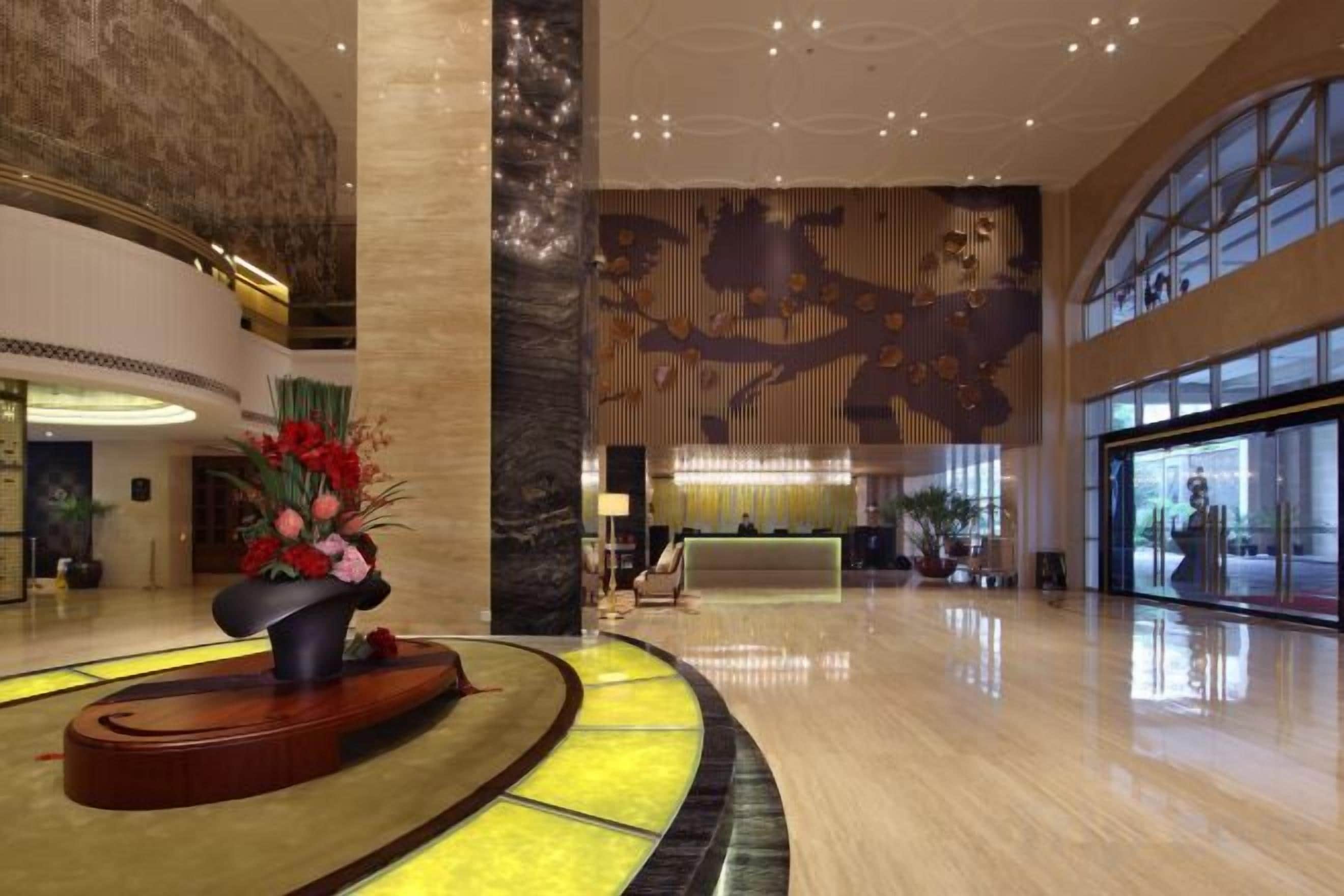 A spacious lobby with a reception desk, a large decorative wall, and a curved seating area with a flower arrangement.