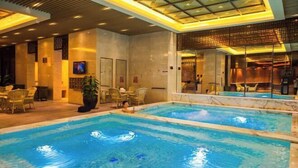 An indoor swimming pool with clear water, surrounded by lounge chairs and a modern ceiling design. - Zhongshan Yihe Junli Hotel (Holiday Plaza Branch) (Zhongshan)