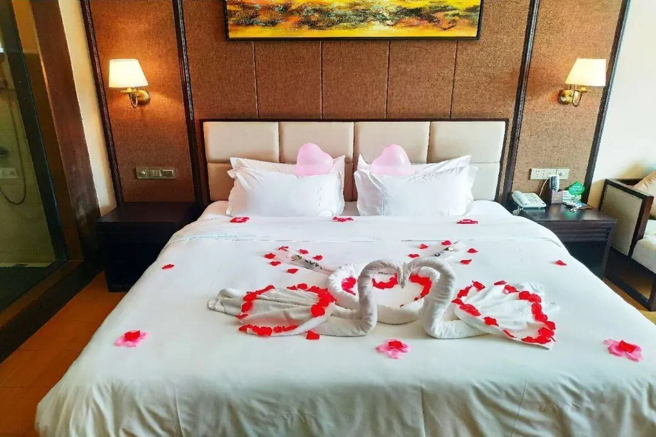 A hotel room with a large bed, two pillows, a nightstand with a lamp, and a painting on the wall.
