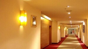 Un couloir d’hôtel avec un tapis rouge, des lampes fixées au mur et des tableaux encadrés.