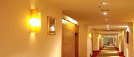 A hotel corridor with a red carpet, wall-mounted lights, and framed pictures.