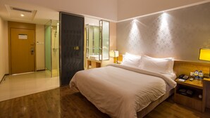 Une chambre d’hôtel avec un grand lit, une table de chevet avec une lampe, une petite table de nuit avec un téléphone et des bouteilles d’eau, une douche en verre et un plancher en bois.