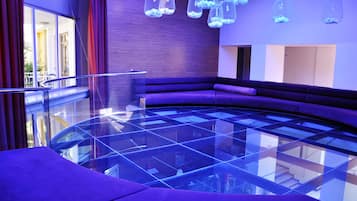 A modern interior with a glass floor, purple seating, and hanging light fixtures.