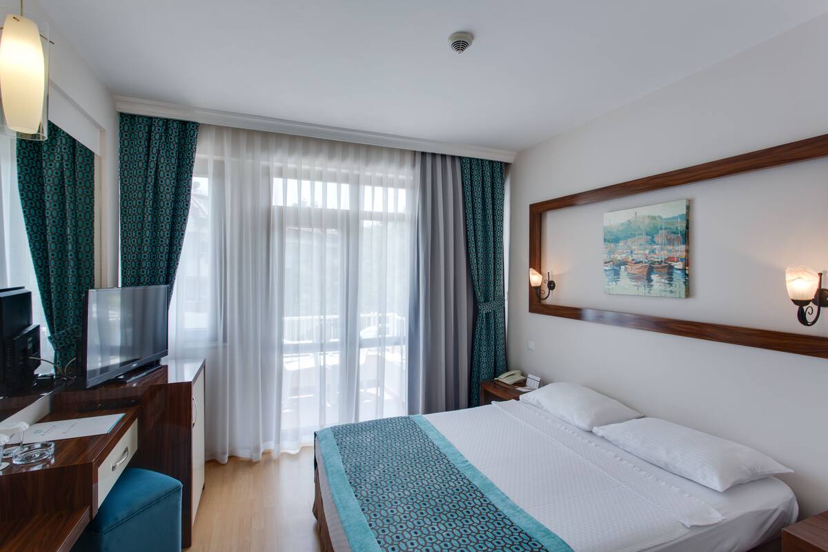 Ein Hotelzimmer mit Bett, Schreibtisch mit Fernseher, Telefon und einem Bild an der Wand.