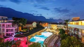 A hotel with a swimming pool, multiple balconies, and a view of mountains.