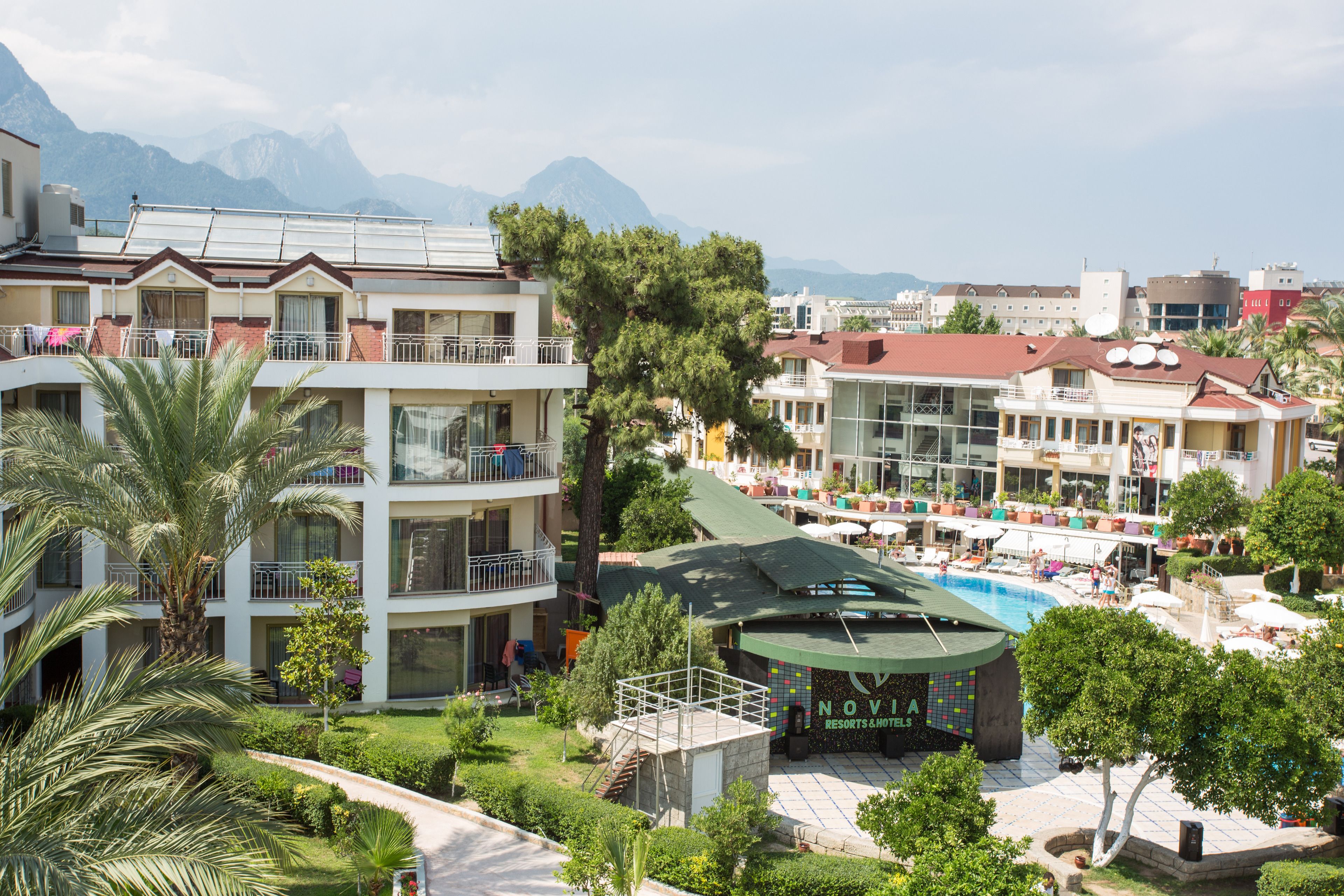 A hotel with multiple balconies, a swimming pool, and a mountainous backdrop.