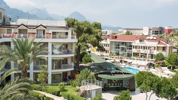 A hotel with multiple balconies, a swimming pool, and a mountainous backdrop.
