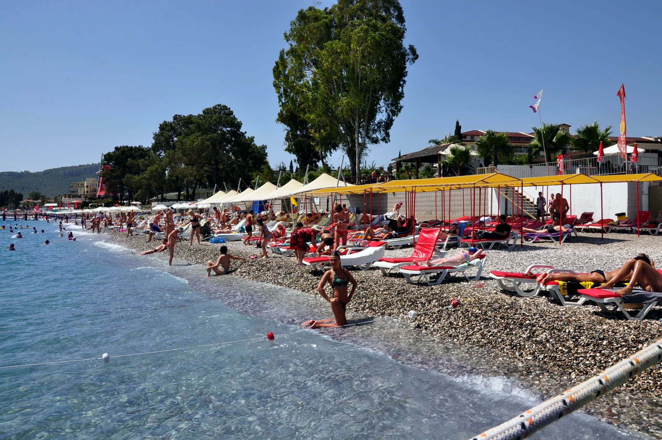 A beach with clear water, people sunbathing, and umbrellas.
