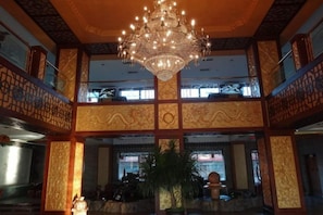 A multi-level interior with ornate wall designs, a central chandelier, and a seating area with a plant. - Beizhen Hotel (Beizhen)