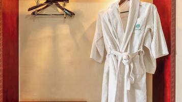 Um robe branco pendurado em um suporte em um quarto com piso de madeira e cortinas vermelhas.
