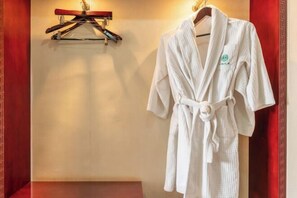 A white robe hanging on a rack in a room with wooden flooring and red curtains. - Beizhen Hotel (Beizhen)