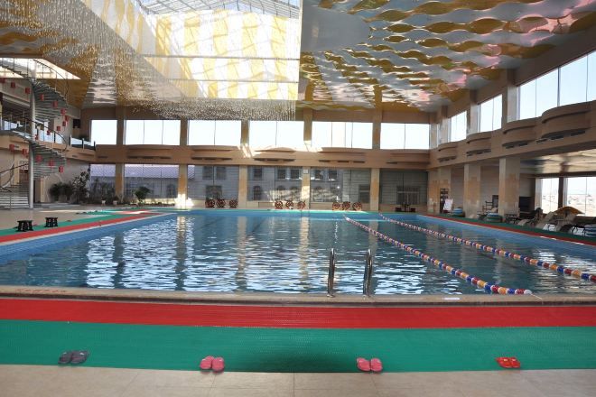 Piscina interior com pistas bem definidas, área de mergulho central e teto alto com padrão único.