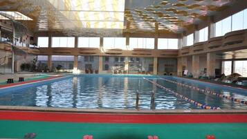 Piscina interior com pistas bem definidas, área de mergulho central e teto alto com padrão único.