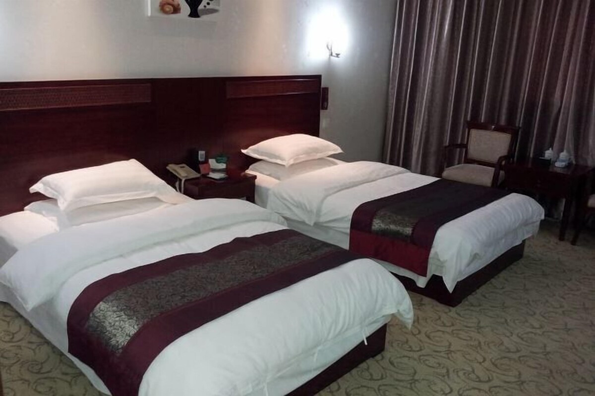 A hotel room with two beds, a wooden headboard, a nightstand with a phone, and a chair.