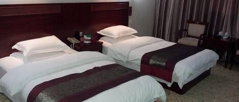 A hotel room with two beds, a wooden headboard, a nightstand with a phone, and a chair.