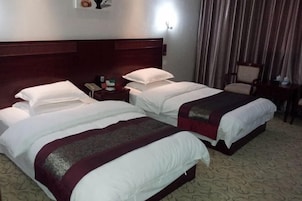 Quarto de hotel com duas camas, um painel de cabeceira de madeira, uma mesa de cabeceira com telefone e uma cadeira.