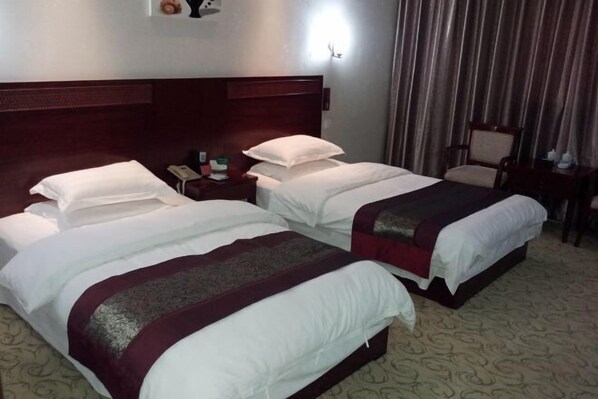 A hotel room with two beds, a wooden headboard, a nightstand with a phone, and a chair.