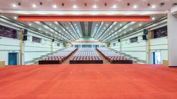 A large indoor auditorium with rows of seats, a stage at the front, and a red carpeted floor.
