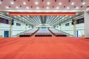 A large indoor auditorium with rows of seats, a stage at the front, and a red carpeted floor. - Beizhen Hotel (Beizhen)