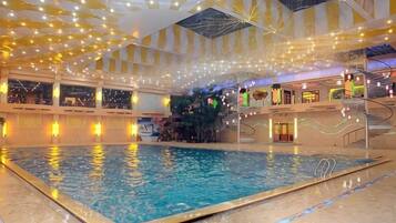 An indoor swimming pool with a central fountain, surrounded by multiple levels of balconies and a ceiling adorned with lights.