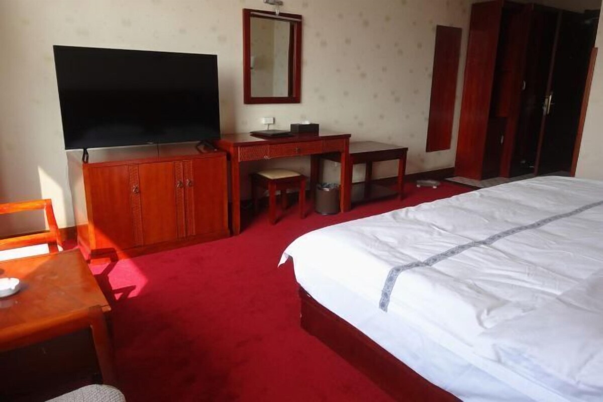 A hotel room with a large bed, a desk with a chair, a television, and a wardrobe.