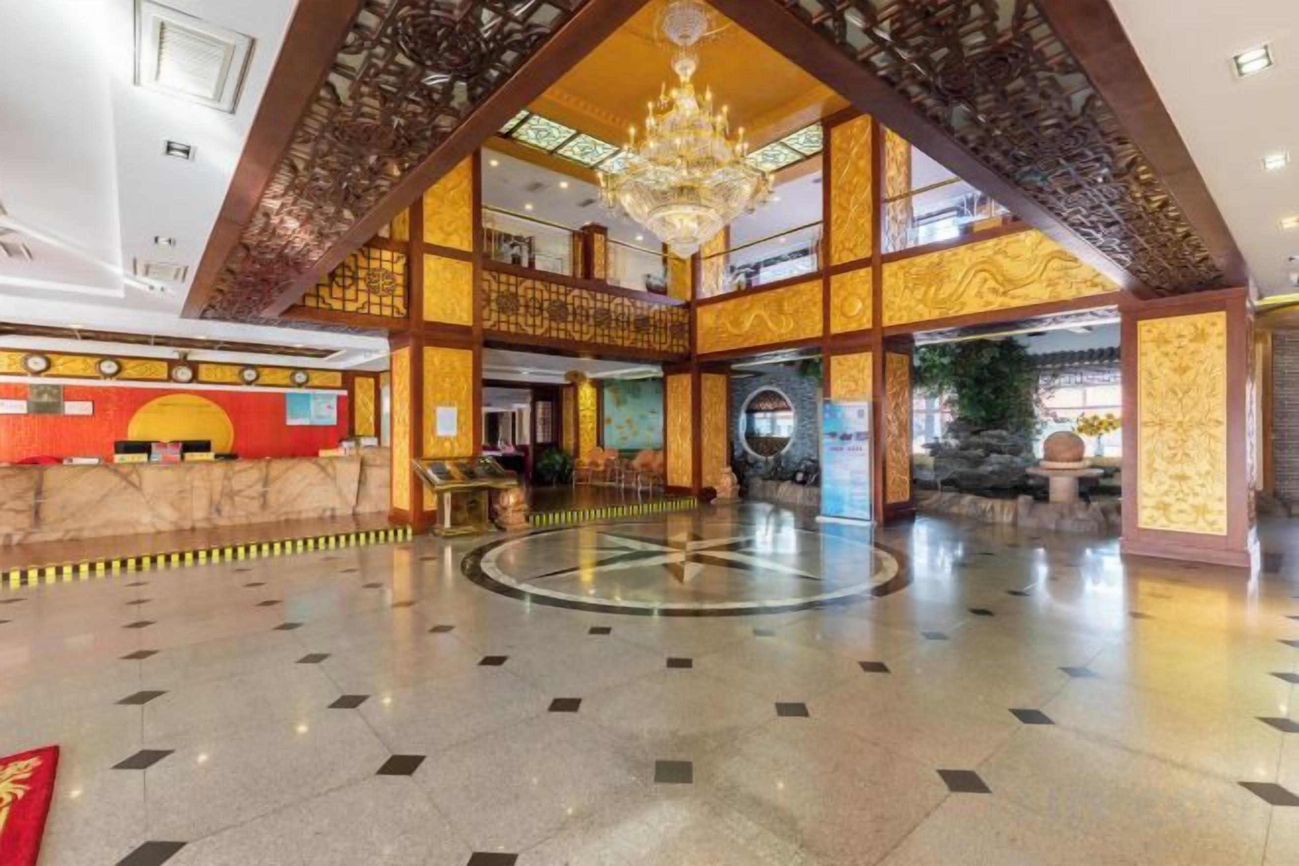 A spacious lobby with a high ceiling, a central chandelier, and a reception desk.