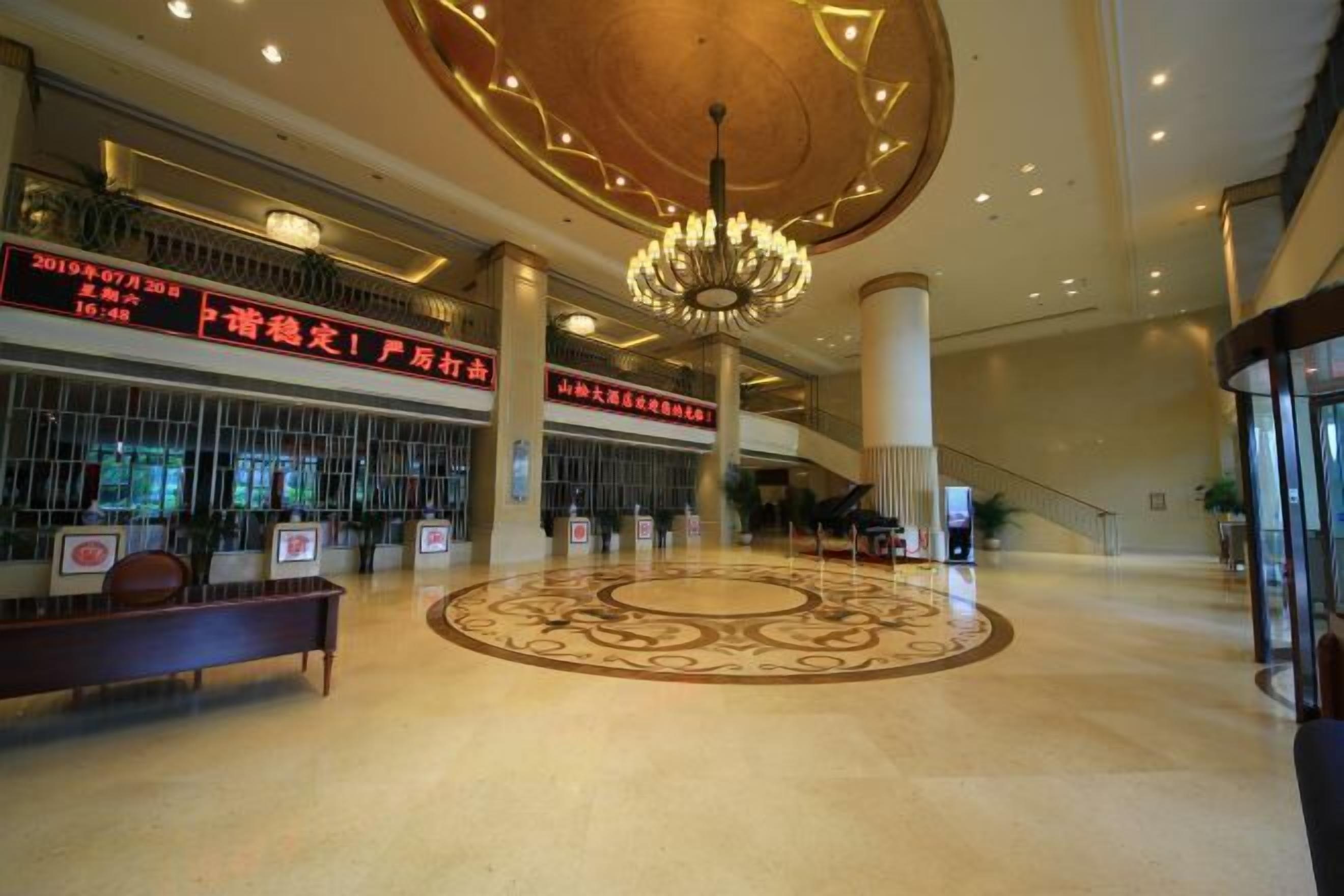 A spacious lobby with a central circular decorative floor pattern, a grand chandelier, and multiple signs with red text.