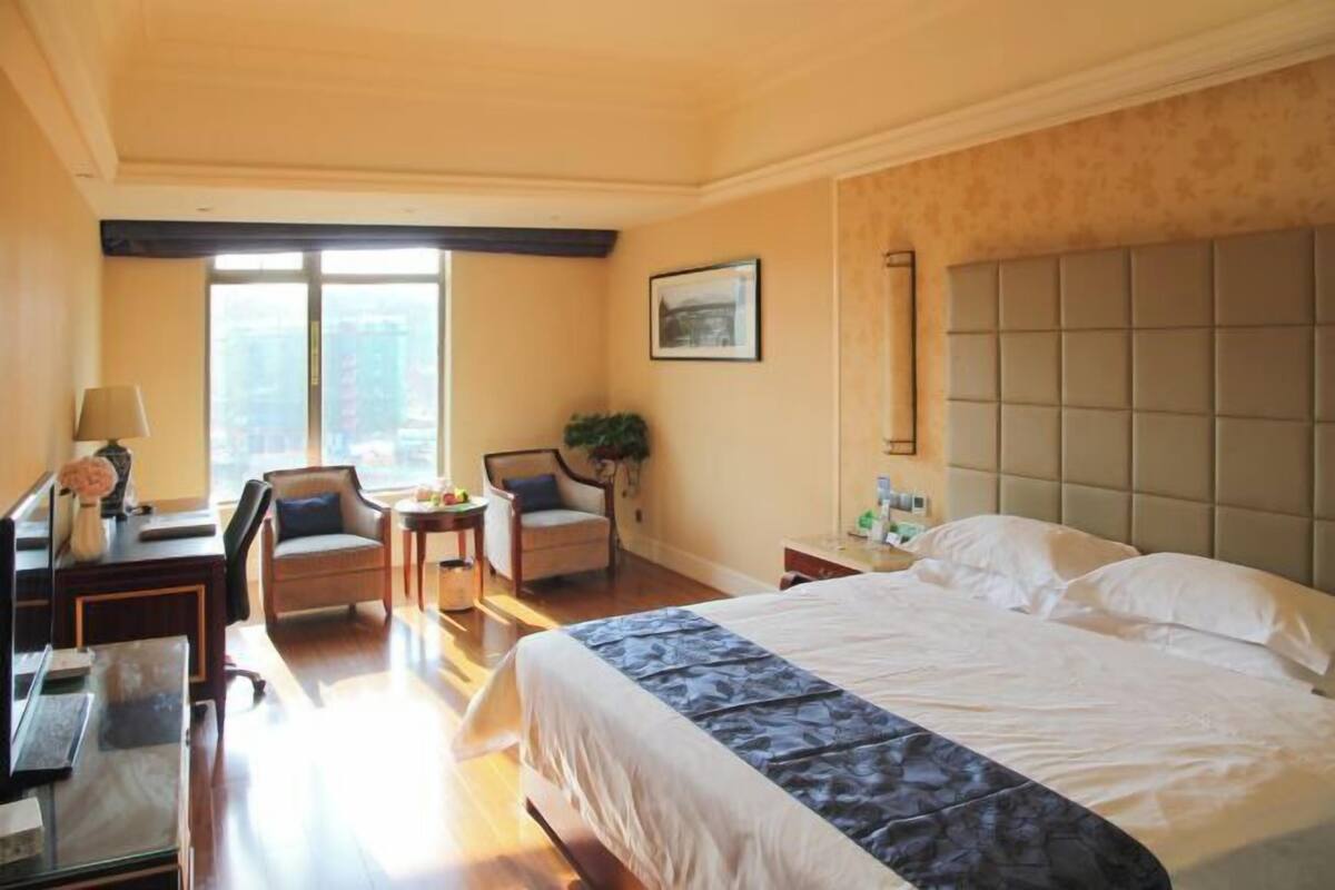 Ein Hotelzimmer mit einem großen Bett, einem Schreibtisch, einem Stuhl, einem kleinen Tisch und einem Fenster mit Blick auf Gebäude.
