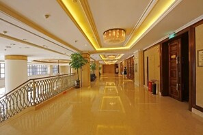Een hotelgang met een gepolijste vloer, een kroonluchter en een kamerplant.