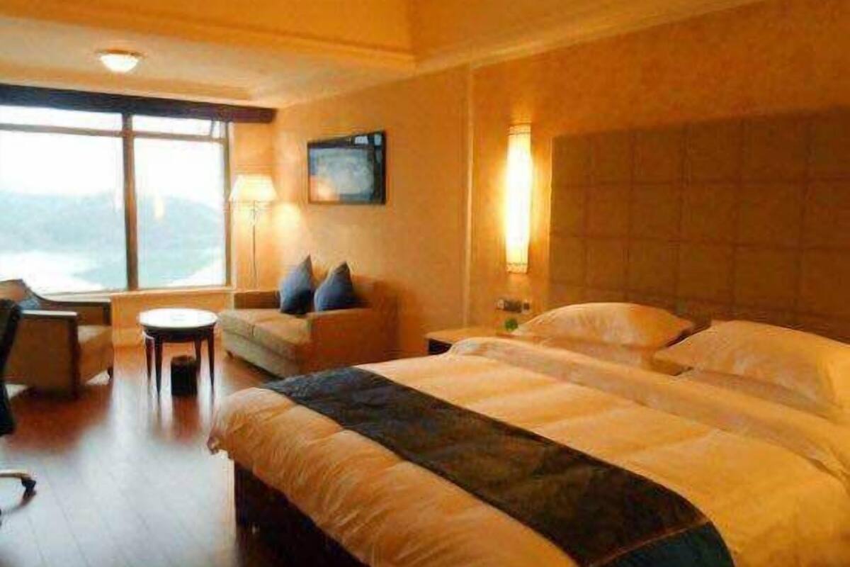 Ein Hotelzimmer mit zwei Betten, einem Sofa, einem Schreibtisch und einem großen Fenster.
