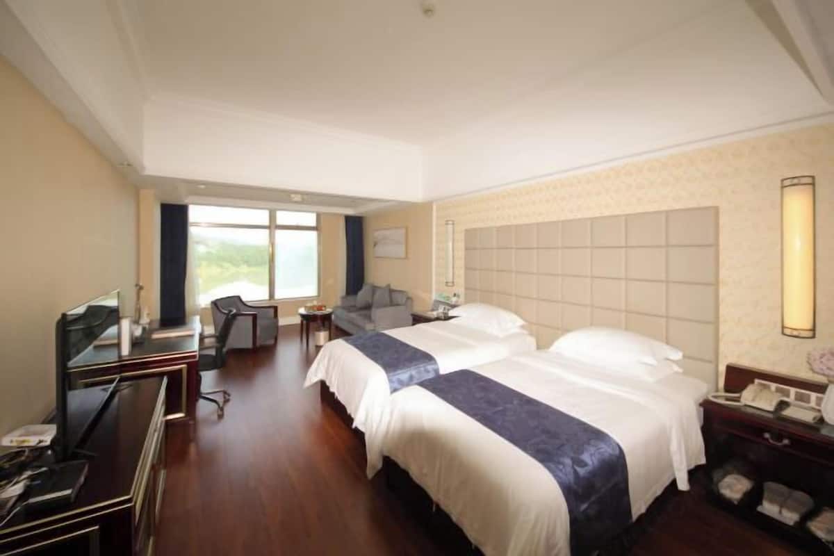 Ein Hotelzimmer mit zwei Betten, einem Schreibtisch, einem Stuhl, einem Fernseher und einem Fenster.