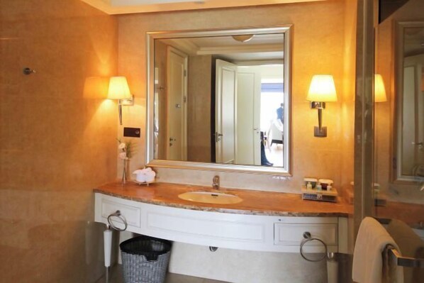 Une salle de bain avec un lavabo en marbre, un grand miroir et deux lampes fixées au mur.