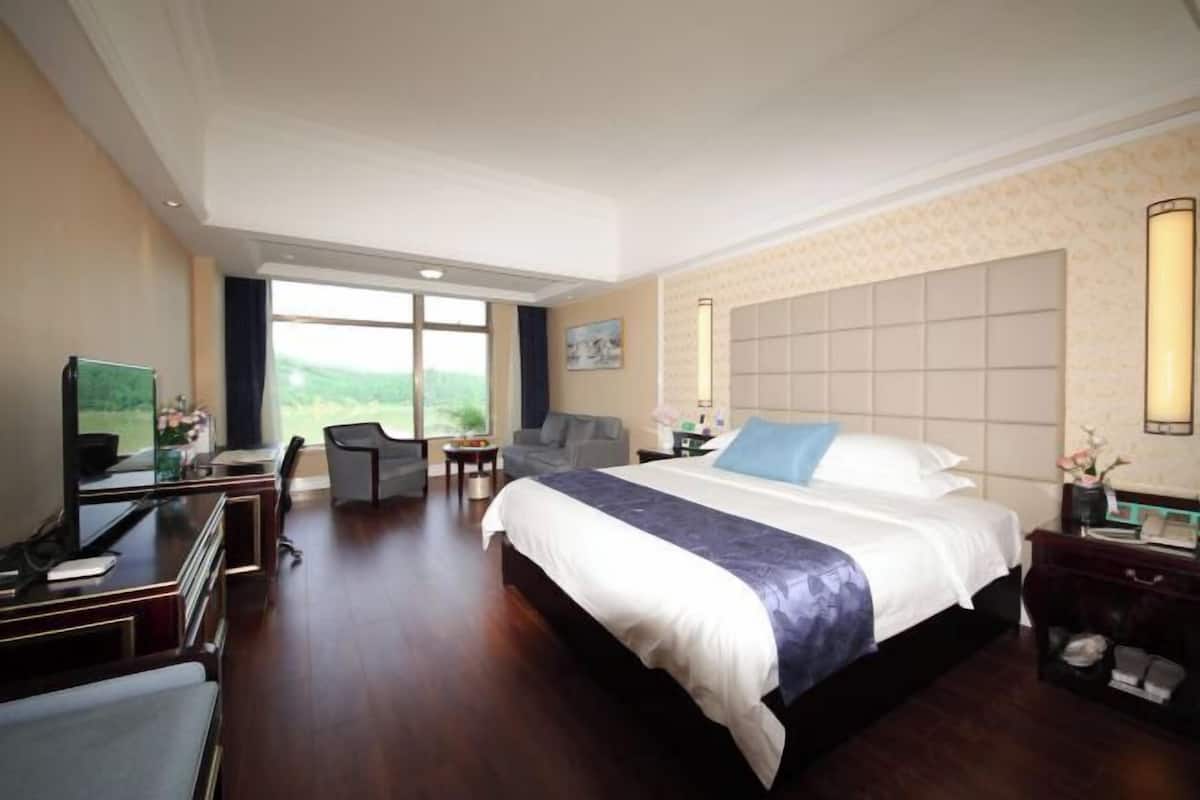 Ein Hotelzimmer mit einem großen Bett, einem Schreibtisch, einem Stuhl und Blick ins Freie.