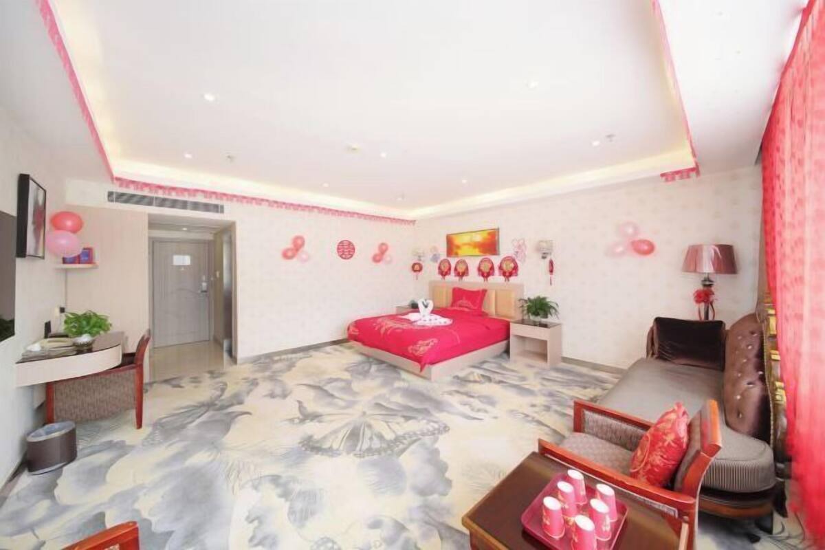A modern bedroom with a large bed, a sofa, a desk, and a red accent wall.