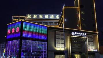 A hotel with a modern facade, featuring illuminated signage and a structured design.
