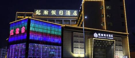A hotel with a modern facade, featuring illuminated signage and a structured design.