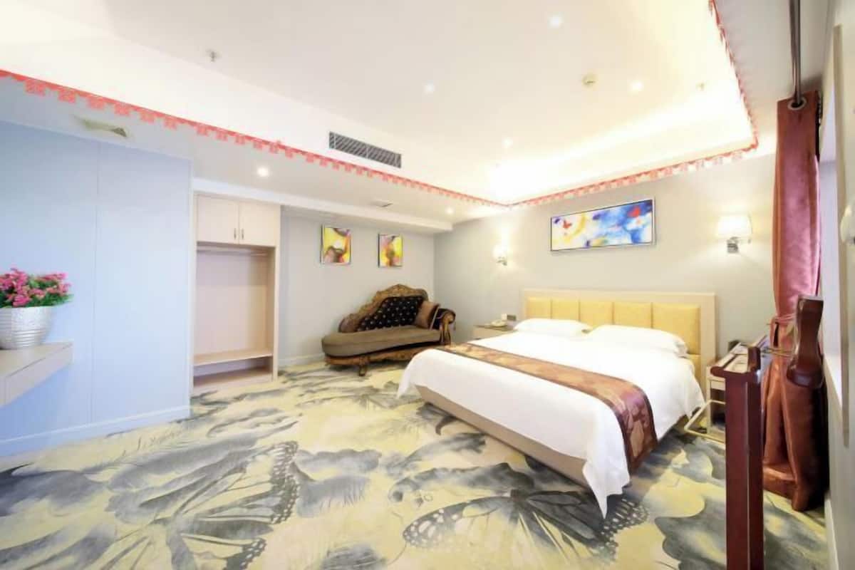 A hotel room with a bed, a sofa, a nightstand, and a wall-mounted lamp.