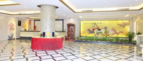 Vestíbulo de hotel con mostrador de recepción, un pilar grande y un mural con caballos.