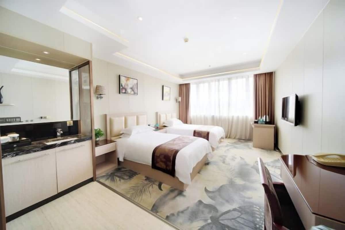 A hotel room with two beds, a large mirror, a flat-screen TV, a desk, and a bathroom with a toilet and sink.