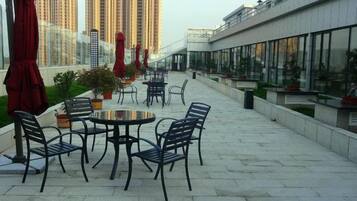 An outdoor patio with tables and chairs, potted plants, and a view of tall buildings.